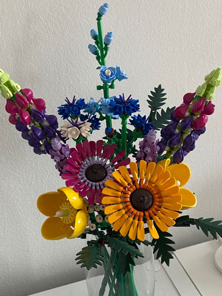 a glass vase filled with colorful flowers on top of a white table next to a wall