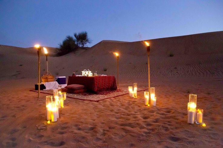 a desert setting with candles lit in the sand and a table set up on it