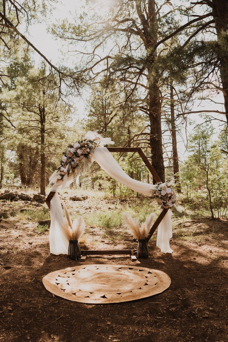 an outdoor wedding arch decorated with flowers and feathers in the woods, surrounded by pine trees