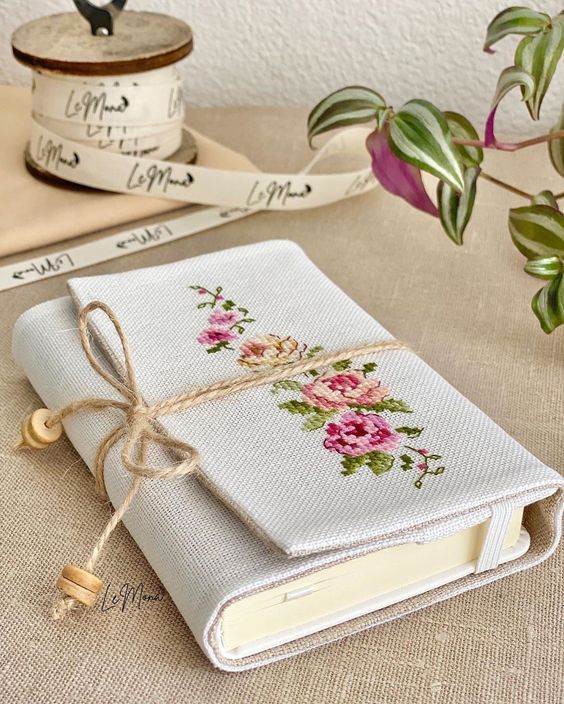 a white book with flowers on it sitting next to some tape and a potted plant