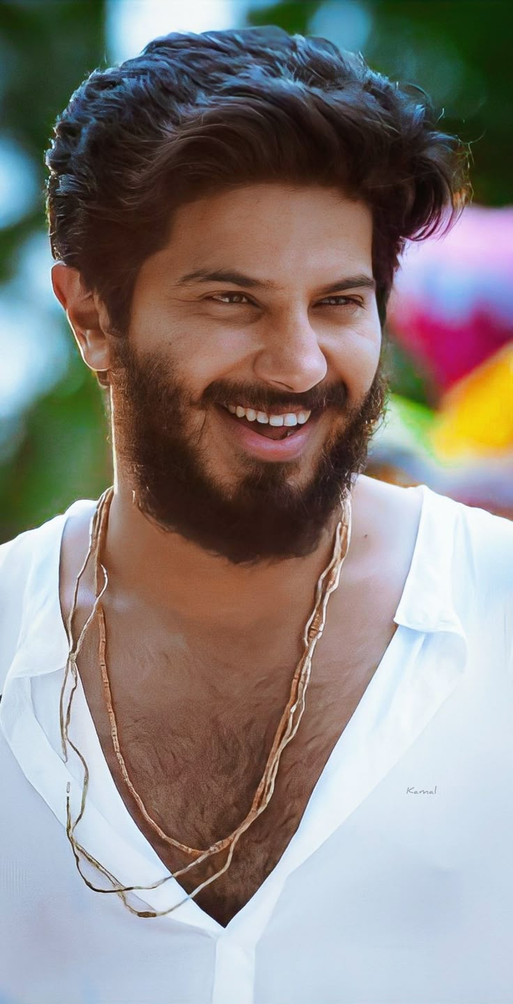 a close up of a person wearing a white shirt and gold necklace with a smile on his face