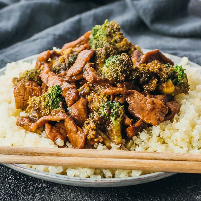 beef and broccoli stir fry over rice on a plate with chopsticks