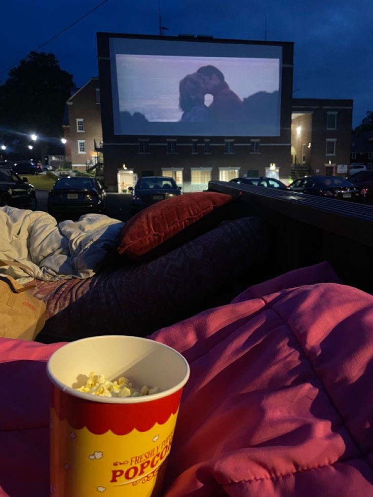 a bucket of popcorn sitting on top of a pink blanket next to a movie screen