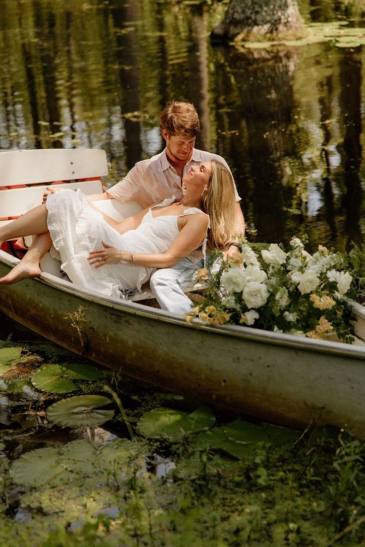 a man and woman sitting in a boat on the water with flowers around them,