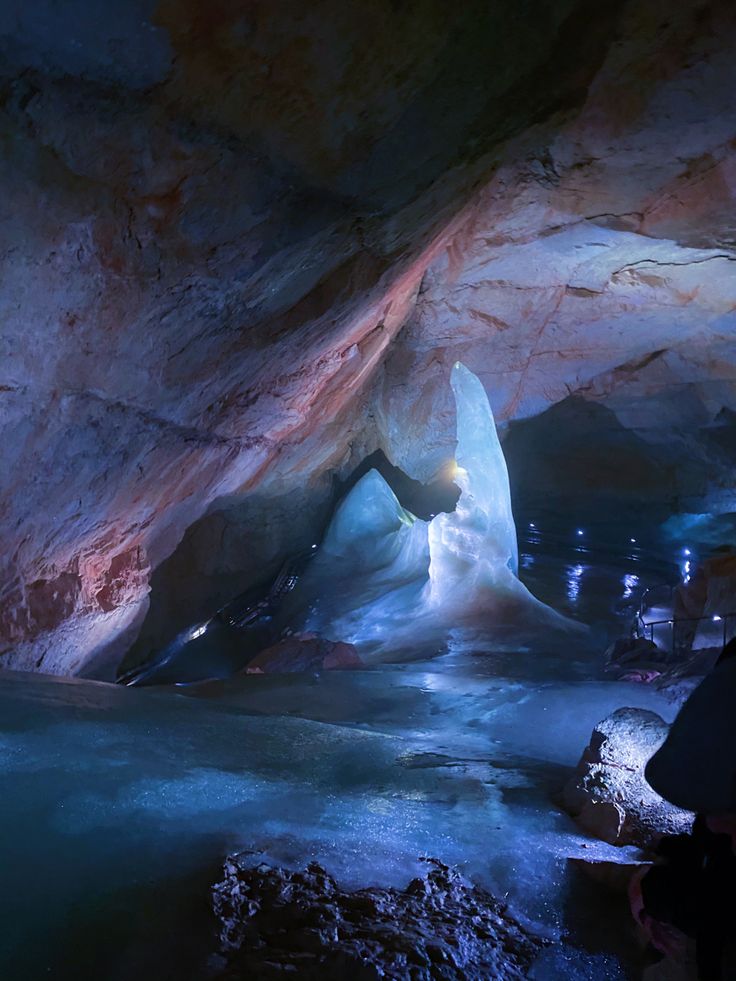 the inside of a cave with blue water and ice on the ground, as well as people standing in it