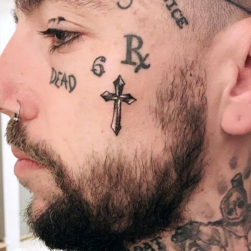 a man with tattoos on his face and cross behind the ear is staring at something