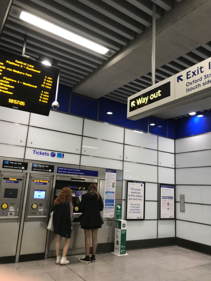 two women are standing in front of an automated ticket machine at the exit into airport