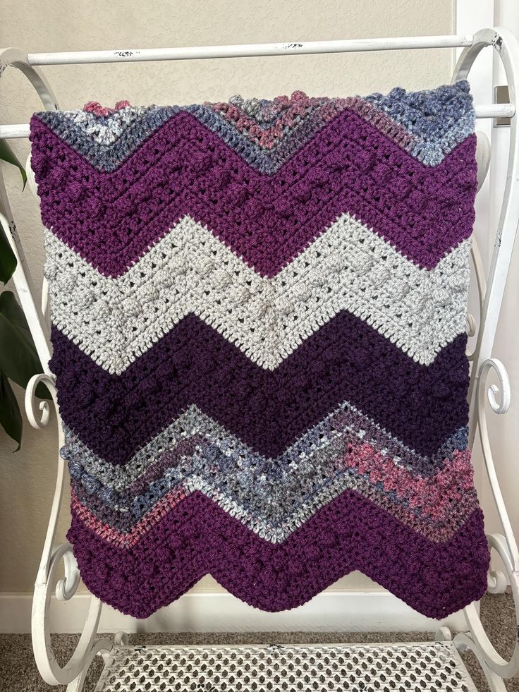 a crocheted blanket sitting on top of a white chair next to a potted plant