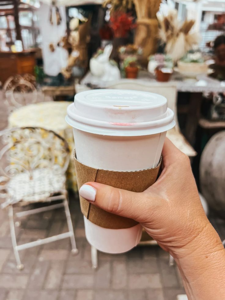 a person holding up a coffee cup in front of a table with chairs and tables