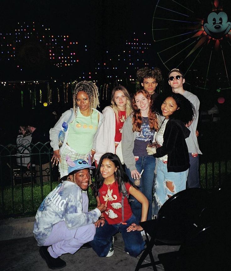 a group of people standing next to each other in front of a ferris wheel at night