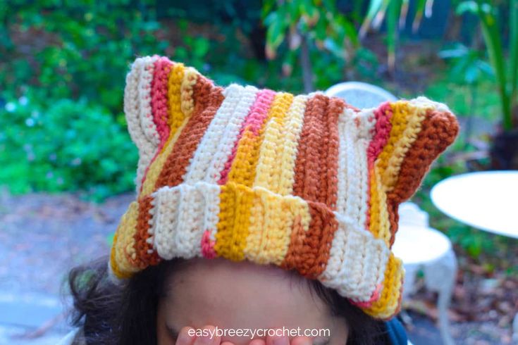 a woman wearing a crocheted cat hat in the backyard with her eyes closed