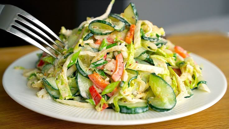 a white plate topped with cucumber and pasta salad on top of a wooden table