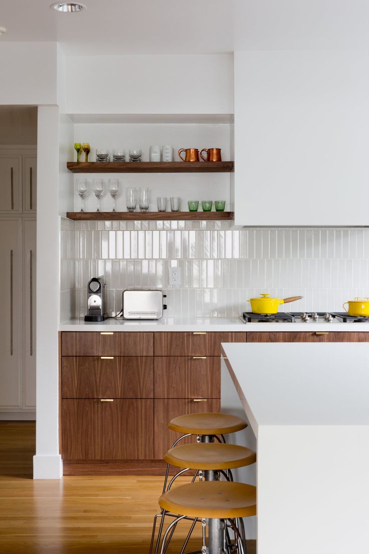 a kitchen with white walls and wooden cabinets, counter tops, and bar stools