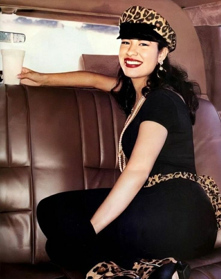 a woman sitting in the back seat of a car holding a cup and smiling at the camera