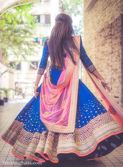 a woman in a blue and pink lehenga is walking down the street with her back to the camera