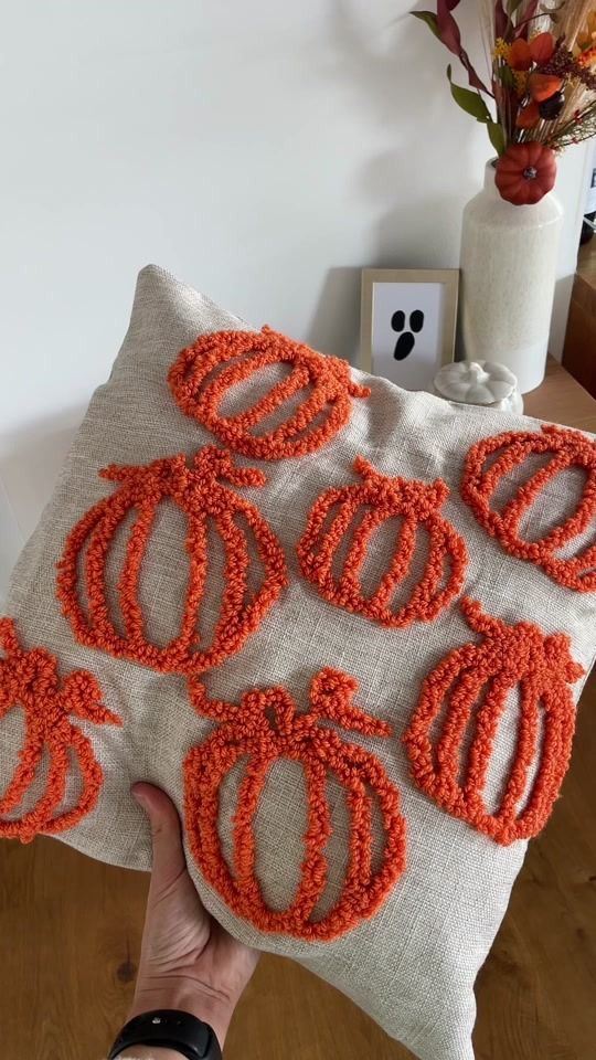 a person holding up a pillow with orange rings on it and some flowers in the background