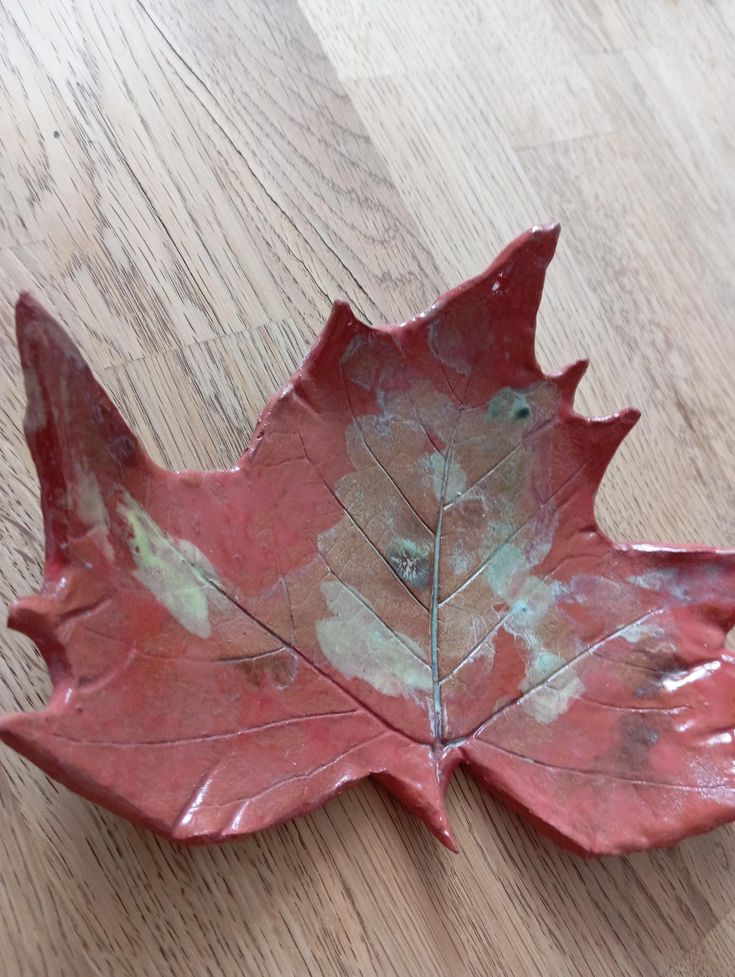 a red leaf shaped dish sitting on top of a wooden table