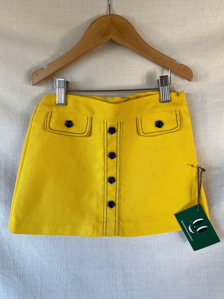 Short vintage 60s trapeze-style skirt in bright yellow, made of frame-style cotton fabric, with buttons and decorative pocket flaps on the front, in the shape of little navy blue flowers, the waistband has an internal elastic for easy putting on and taking off. The cut of the skirt, the contrasting seams in the same tone as the decorative flower buttons are a hymn to love and the flower power of the most hippie decade in history. This skirt, brought directly from London, is a new unsold stock garment and is in perfect condition except for a few small rust marks on the waistband because after all it is a piece that has more than 50 year of paitently waiting for an owner (please do feel free to ask for more photos and details of this). It is a very colorful and very swinging London garment, Cotton School Skirt For Spring, Cotton Skirt For School In Spring, Cotton Skirt For School During Spring, Spring School Cotton Skirt, Spring Cotton Skirt For School, Retro School Bottoms For Spring, Retro Bottoms For School In Spring, Spring Cotton Skirt With Snap Buttons, Spring School Skirt With Pockets