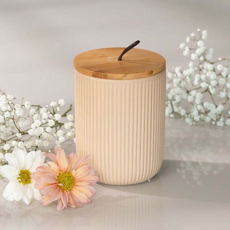 a white vase with a wooden lid next to flowers