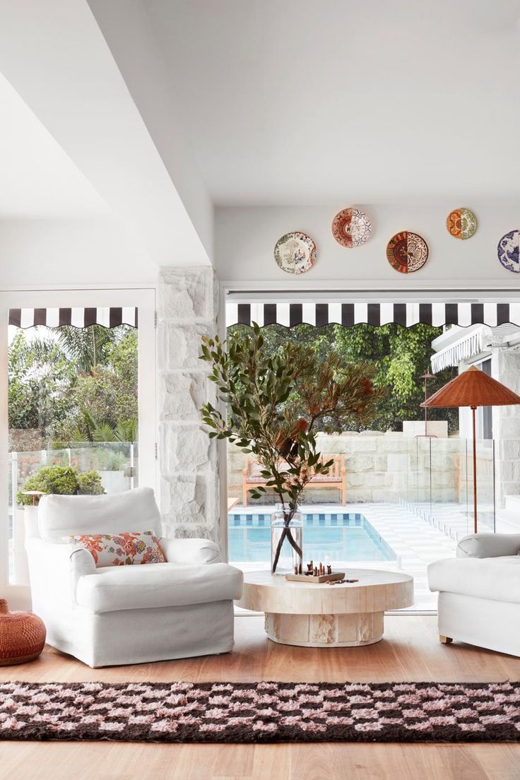 a living room filled with white furniture next to a swimming pool