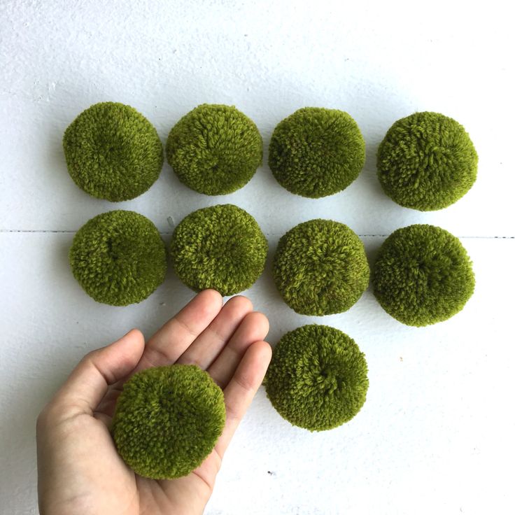 a hand is picking up moss balls from the ground to be placed on top of each other