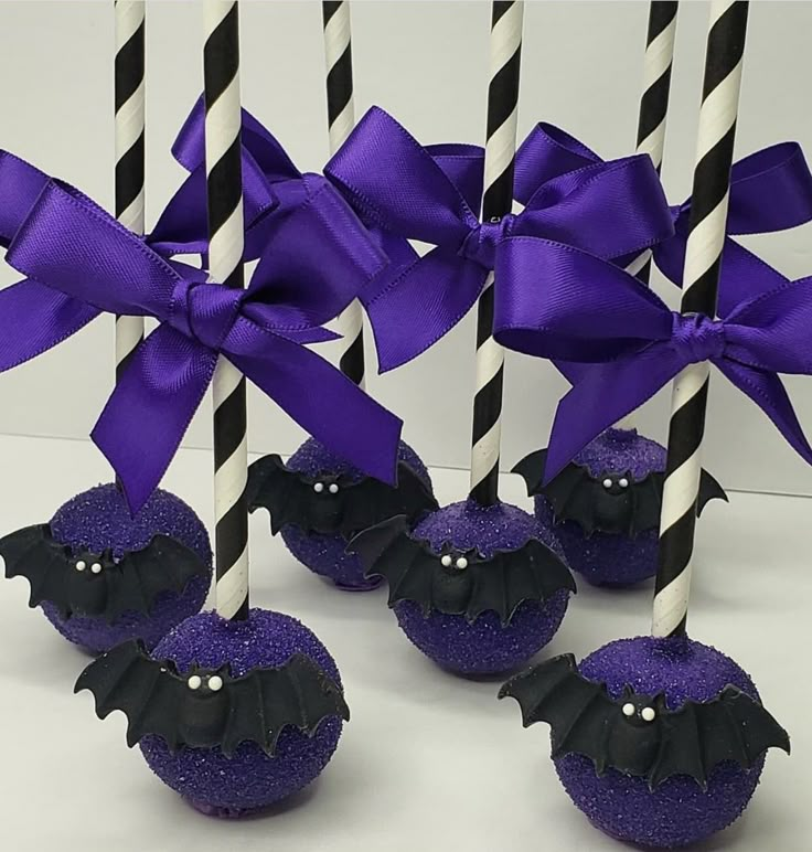 purple and black candy apples with bats on them, tied with ribbons in front of white background