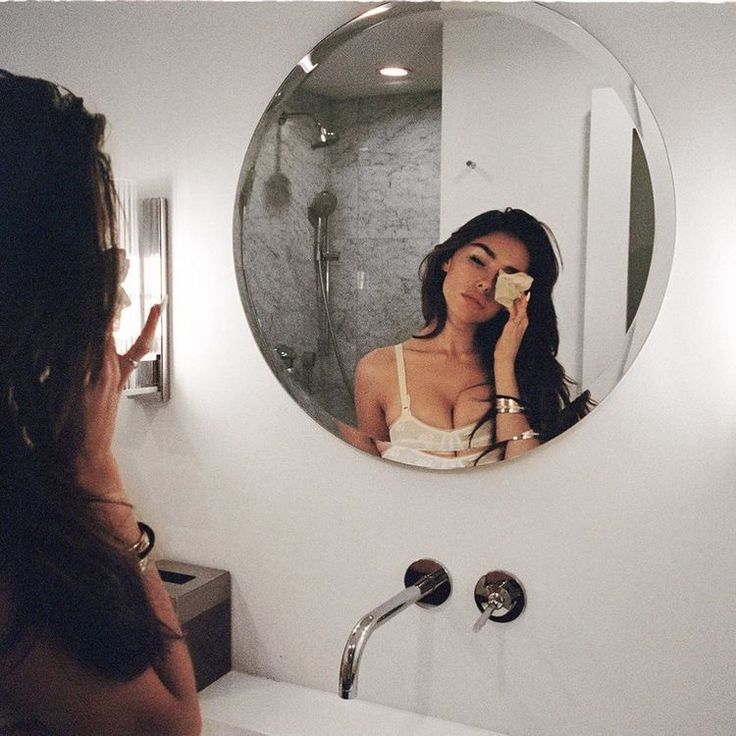 a woman taking a selfie in front of a bathroom mirror while brushing her teeth