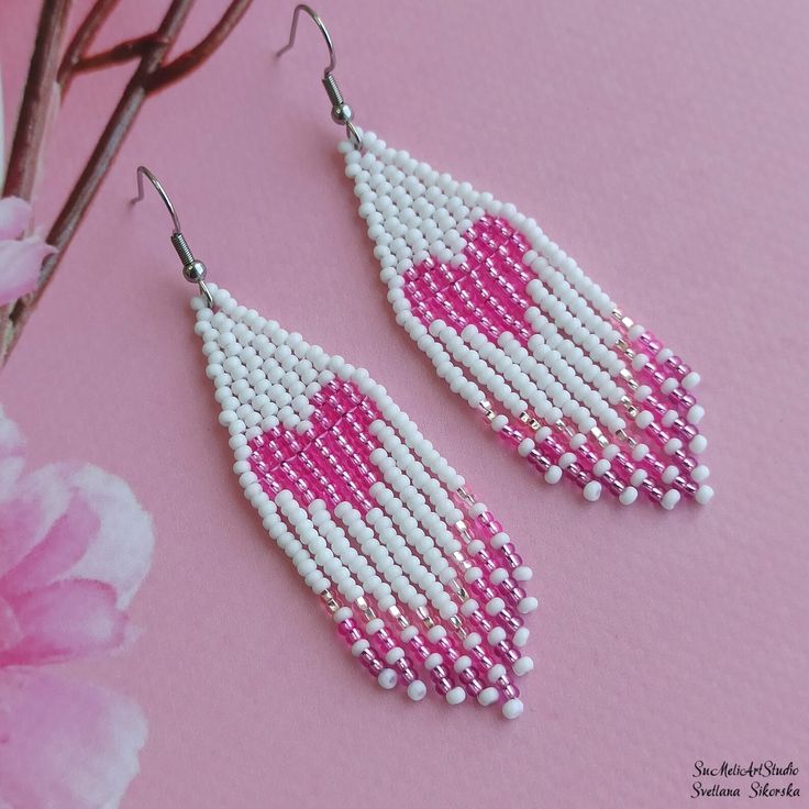 pink and white seed beaded earrings with hearts on them sitting next to a flower