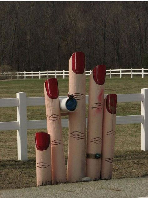 three wooden sticks with faces painted on them in front of a white fence and trees