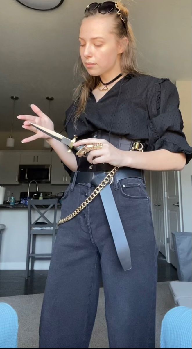 a woman in black shirt and jeans holding a cell phone with chains on her waist