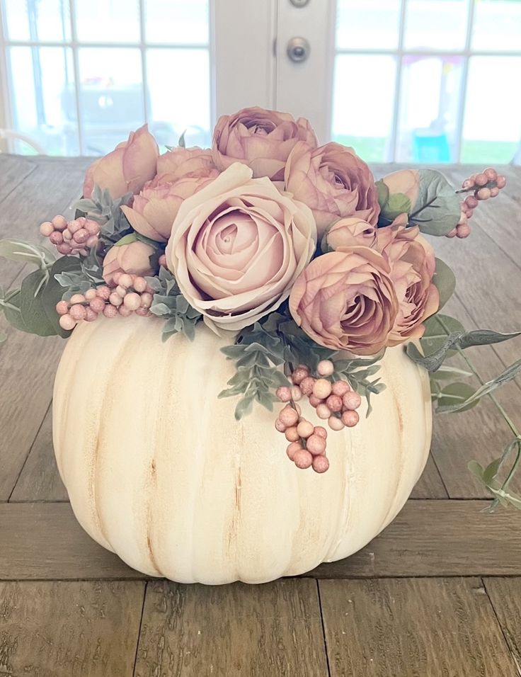 a white pumpkin filled with flowers on top of a wooden floor