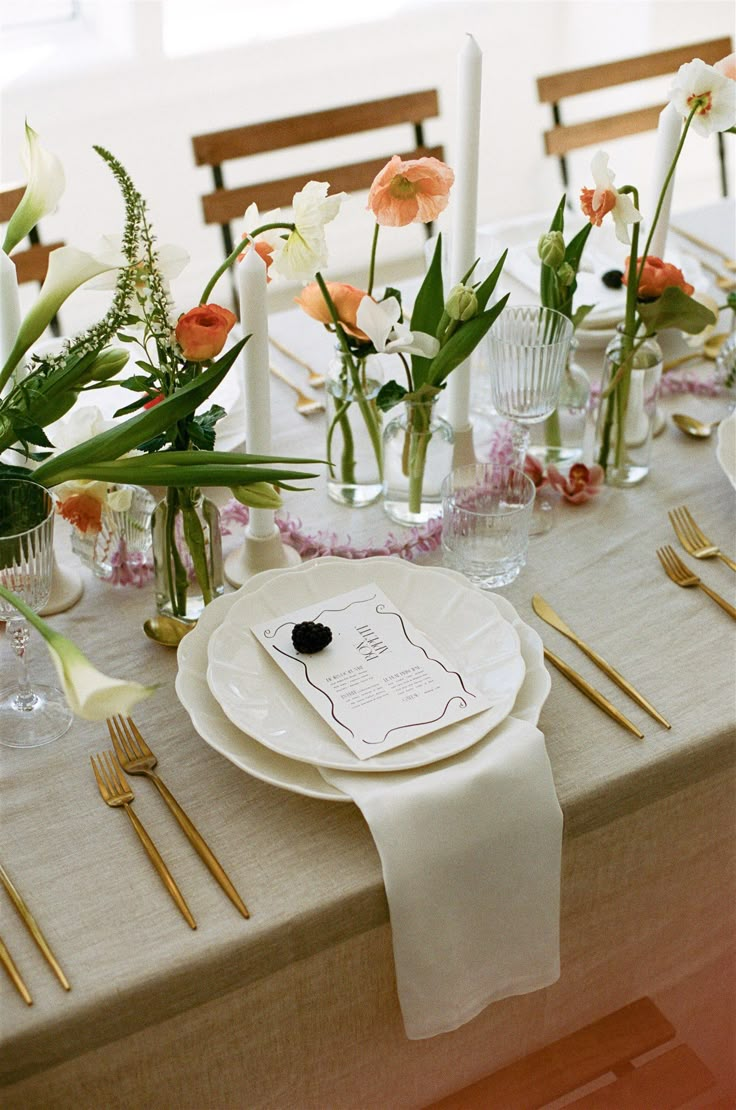 the table is set with white plates and silverware, flowers in vases, and candles