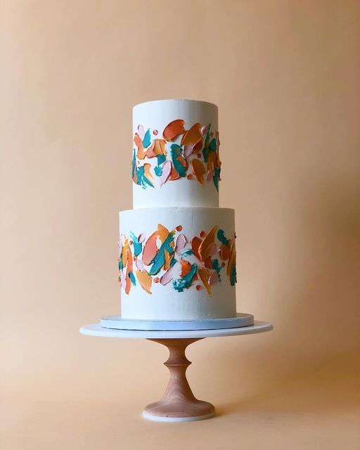 a three - tiered cake decorated with colorful leaves on a white plate against a beige background