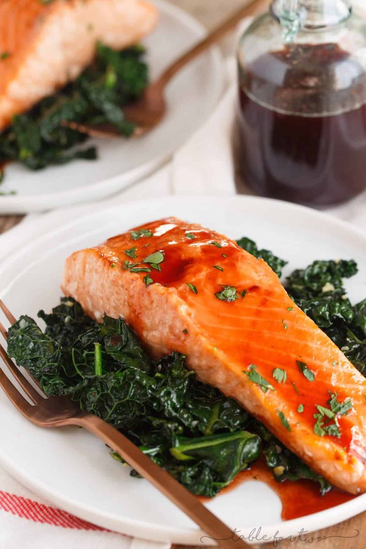 two white plates with salmon and greens on them, one has a fork in it