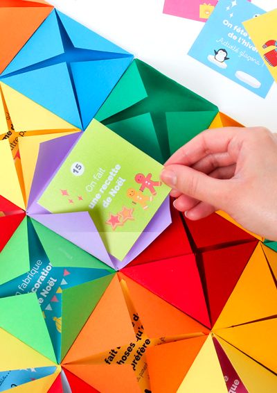 someone is holding an origami card in front of a rainbow colored background with other cards