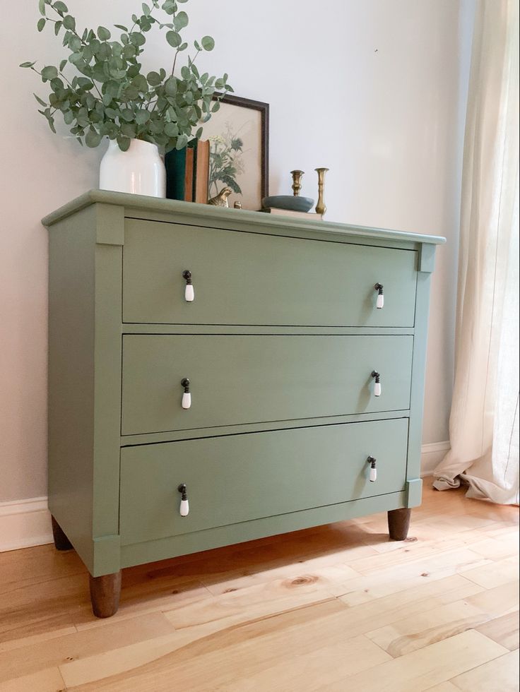 a green dresser sitting on top of a hard wood floor next to a potted plant