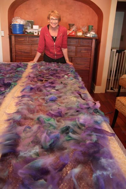 a woman standing in front of a bed covered in purple and green yarn on top of a wooden dresser