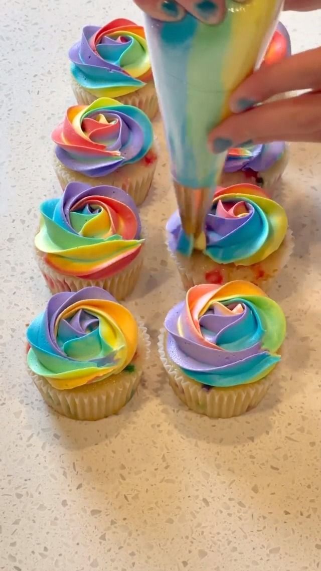 someone is decorating cupcakes with rainbow icing