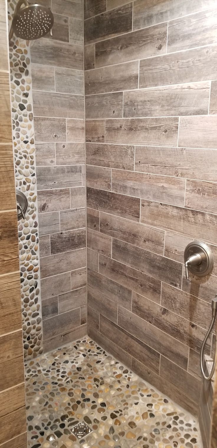 a walk in shower sitting next to a tiled wall and floor covered in pebbles on the ground