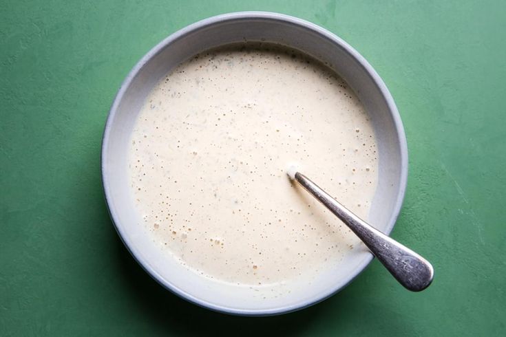 a white bowl filled with liquid and a spoon on a green table top next to it