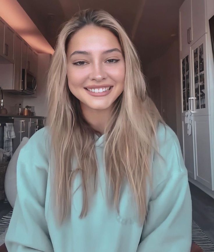 a woman with long blonde hair is smiling for the camera while wearing a blue sweatshirt