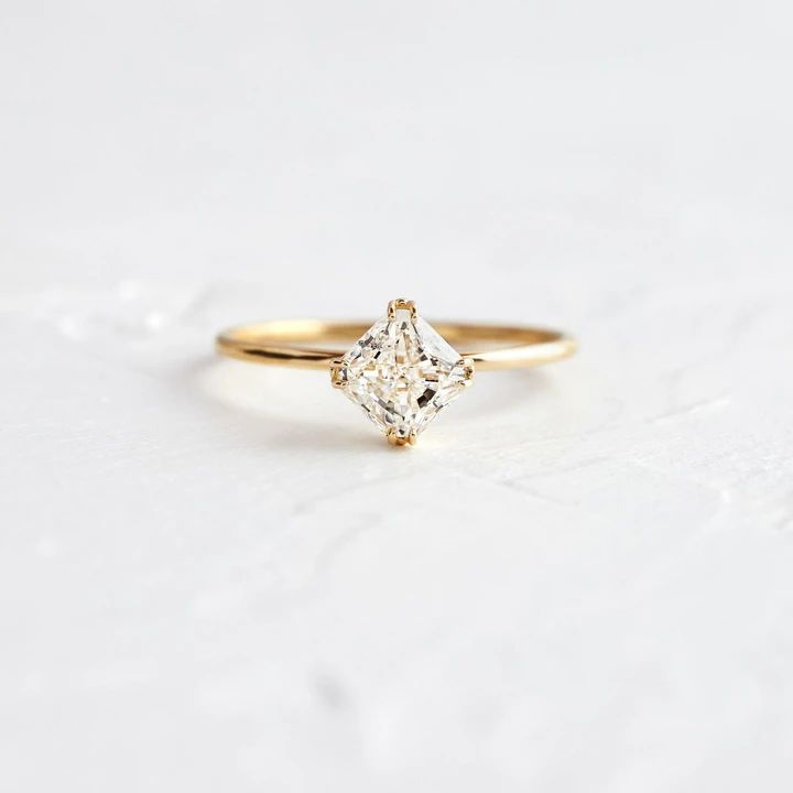 a yellow gold engagement ring with a princess cut diamond in the center on a white background