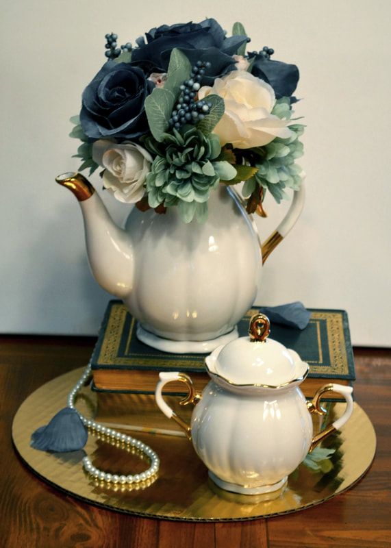 a tea pot with flowers in it sitting on top of a table next to a book