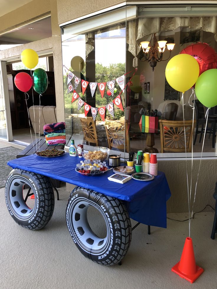 a blue table topped with lots of balloons next to a store front window filled with items