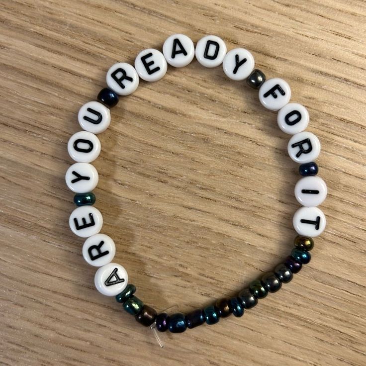 a beaded bracelet that says ready for it on top of a wooden table with beads