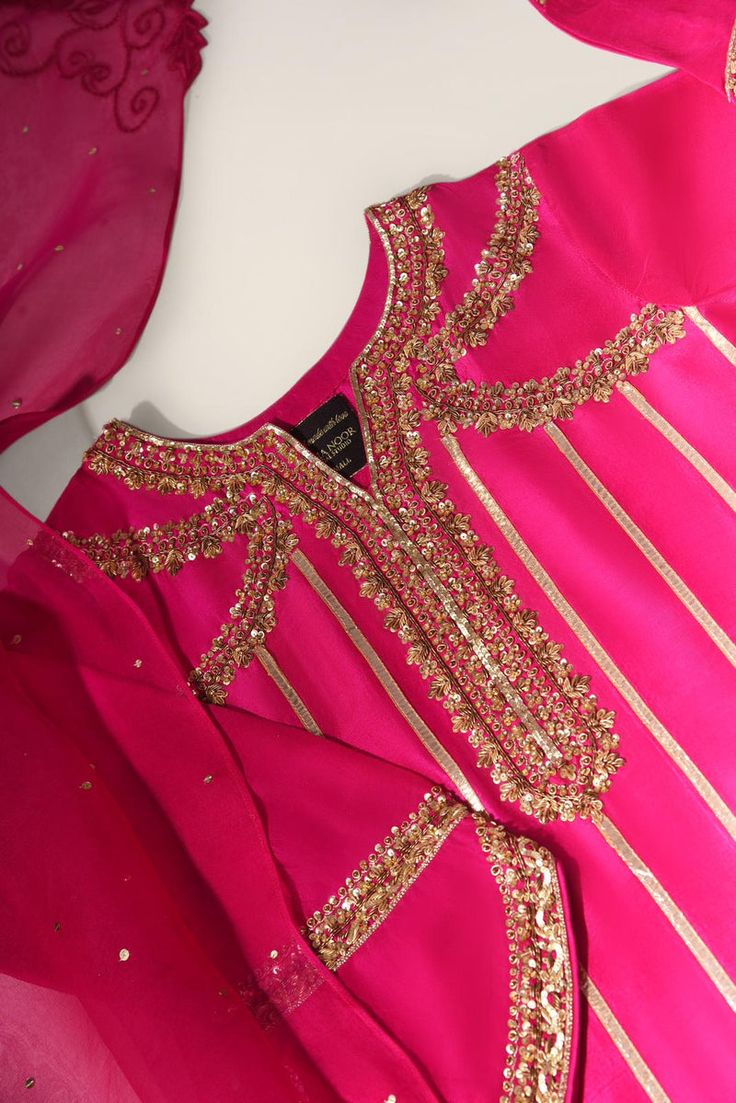 Designed on fuchsia pink pure raw silk 68 gms featuring hand work in gold zardosi, stitched to perfection, an elegant long kameez with straight trousers, paired with a hand crafted pure organza dupatta with gold sequins spray alongside cutwork motifs in four corners. The length of the long kameez is 48 inches. Order Du Party Chanderi Kurta In Gold, Pink Organza Traditional Wear With Dabka, Eid Traditional Wear With Gold Embroidery On Organza, Eid Organza Traditional Wear With Gold Embroidery, Party Gold Chanderi Kurta, Pink Silk Unstitched Suit With Dabka, Pink Organza Kurta With Dabka Embroidery, Pink Raw Silk Unstitched Suit For Party, Gold Organza Churidar With Dabka Work