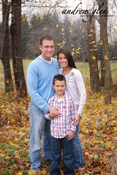 a man and woman standing next to a young boy in the woods with leaves on the ground