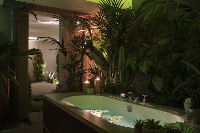 a bathtub with plants and candles lit in the corner, surrounded by greenery