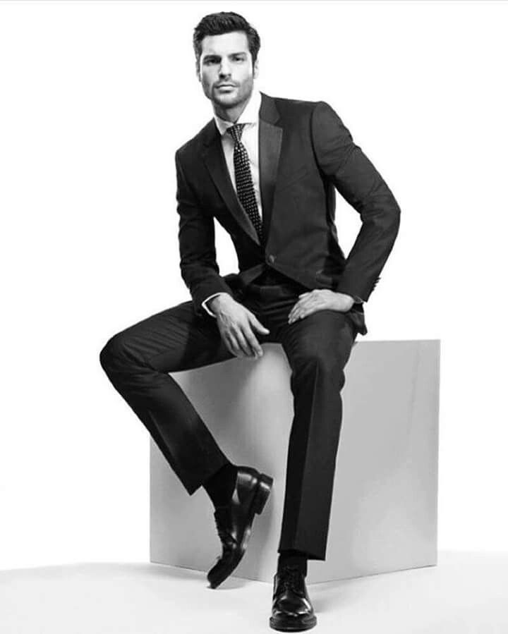 a man in a suit and tie sitting on a white block posing for a black and white photo