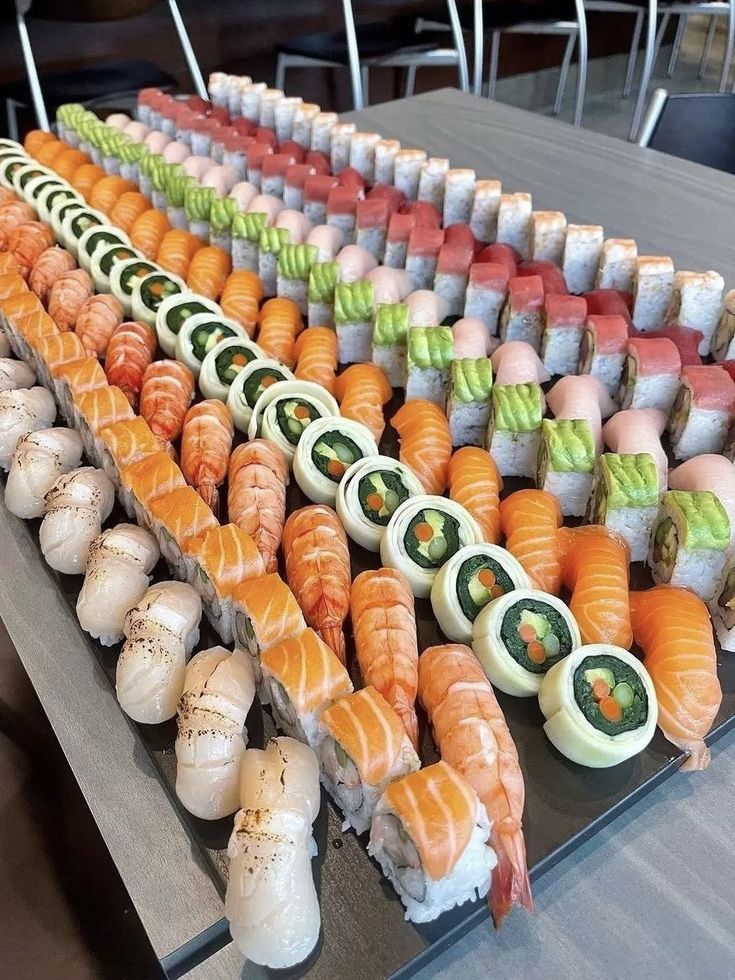 an assortment of sushi is displayed on a long table with chairs in the background